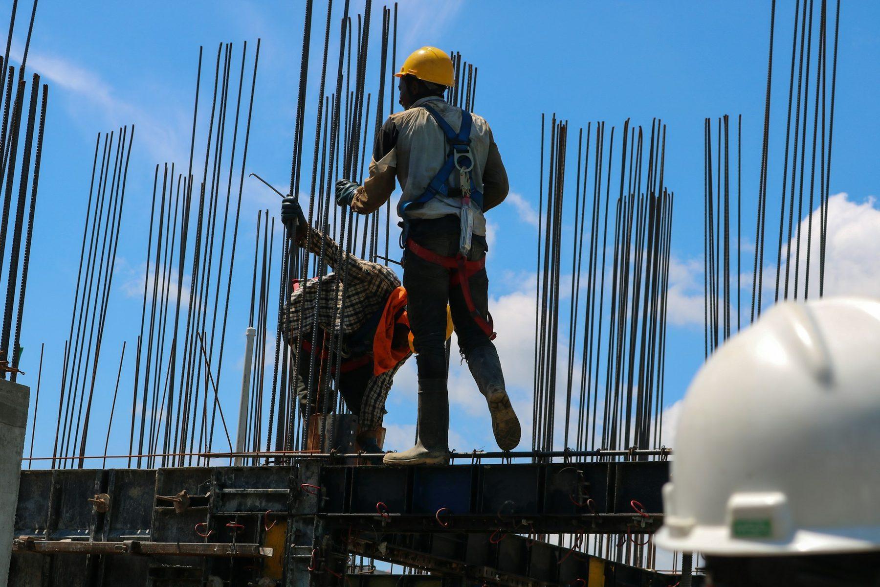 Construction workers in harnesses and hard hats fixing rebar on site under a blue sky