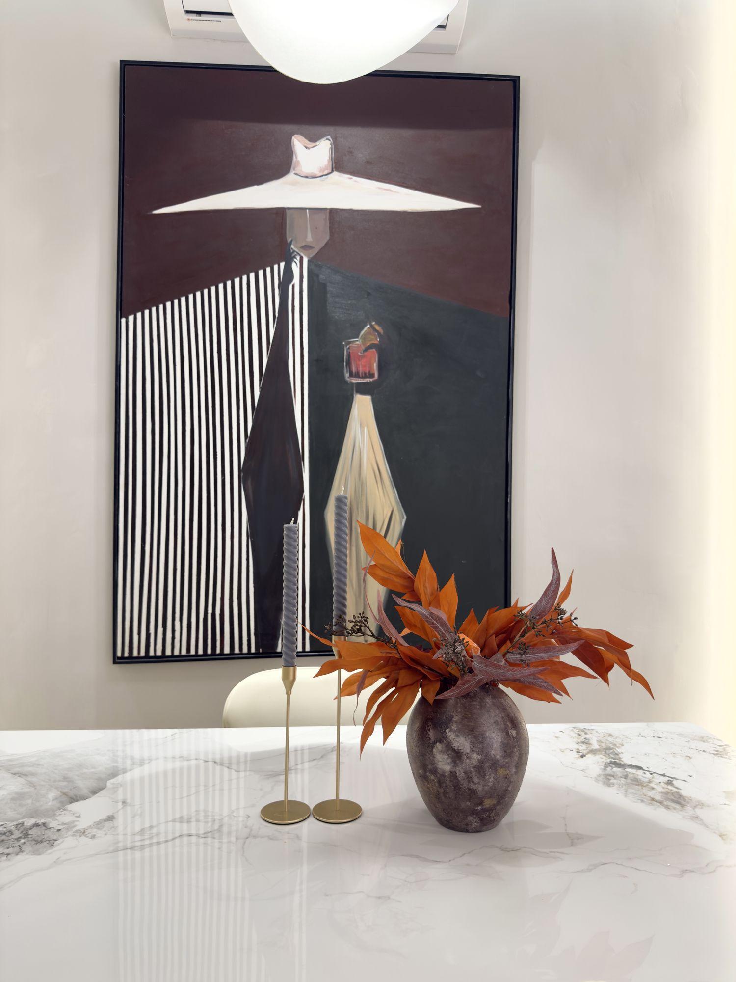 Marble dining table styled with brass candlesticks and autumn leaves beneath the artwork