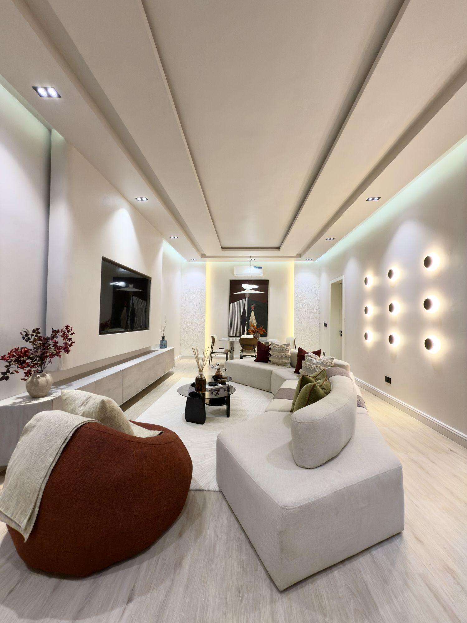 Living room with curved cream sofas, circular wall lights and a coffered ceiling washed in cool light