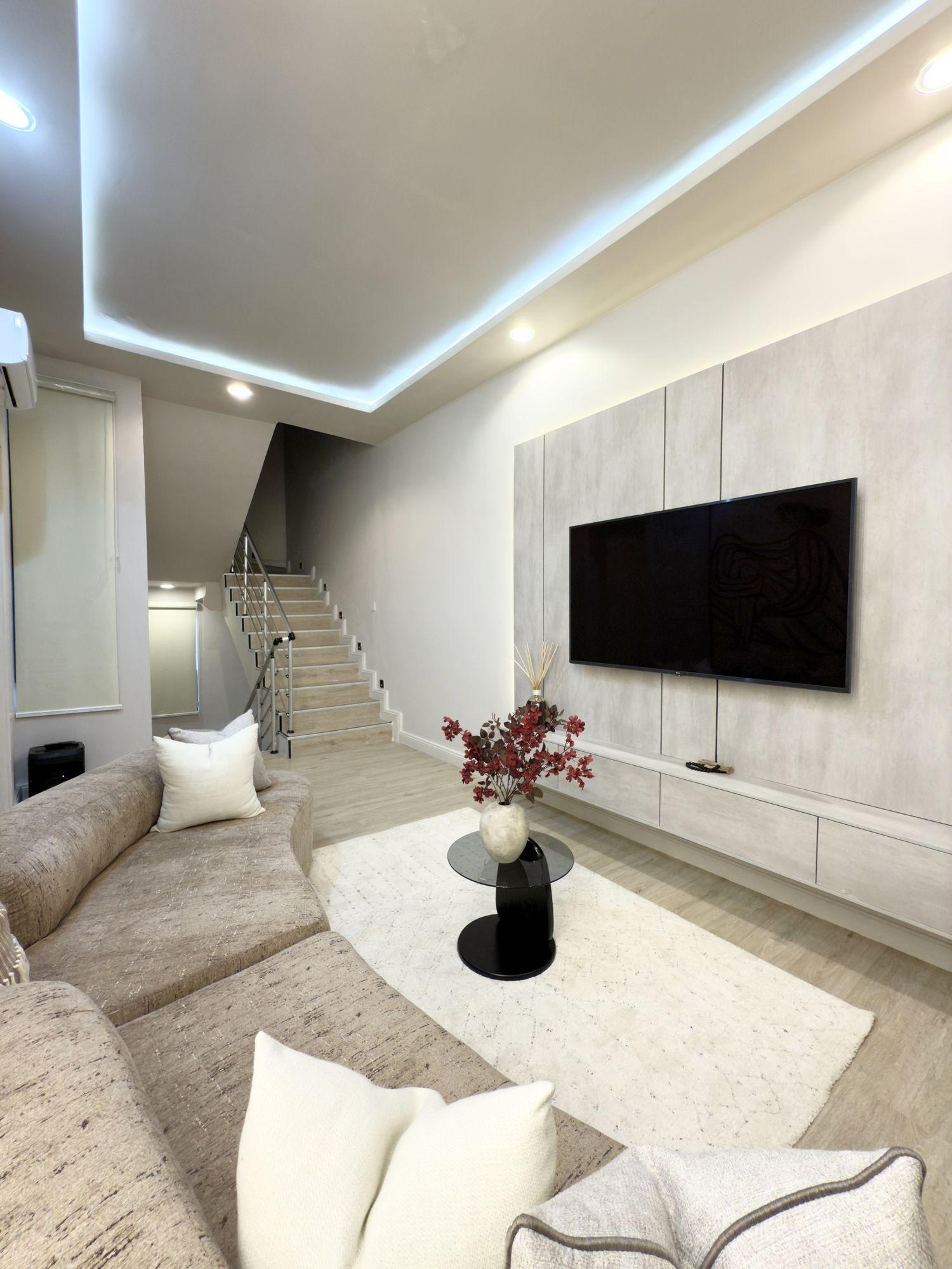 Television lounge with a curved boucle sofa and cove lit ceiling beside the stair