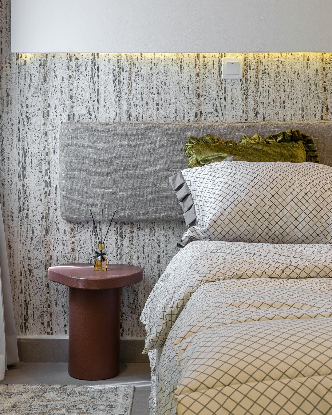 Bedside detail with a rust side table and concealed lighting above the headboard