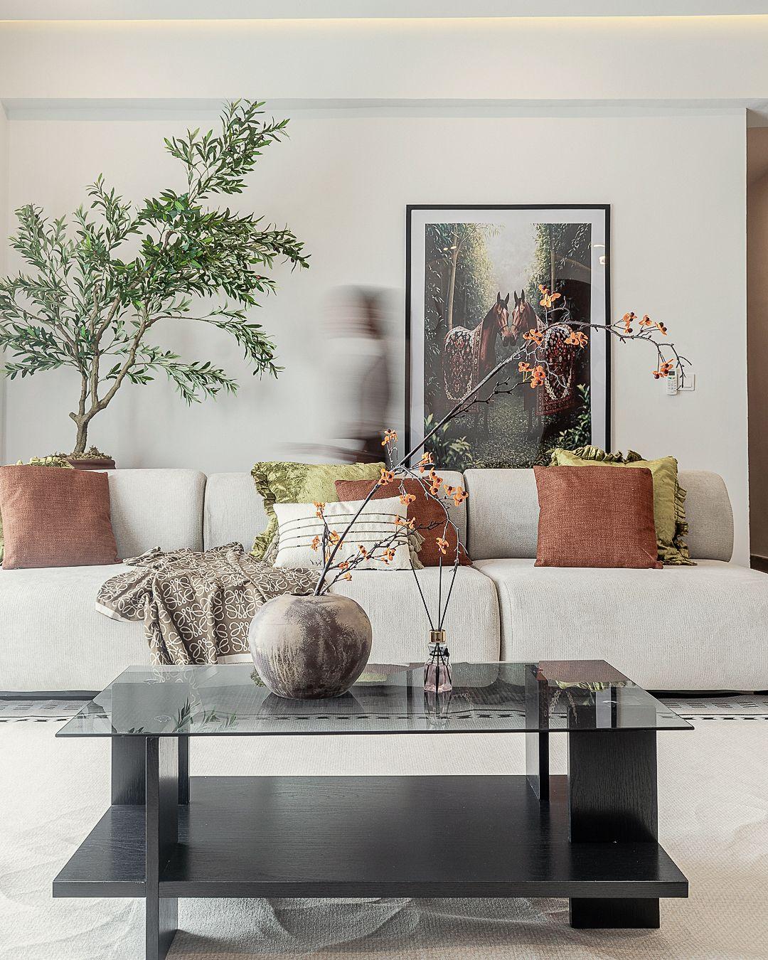 Sofa detail with a black framed glass coffee table and stone vase