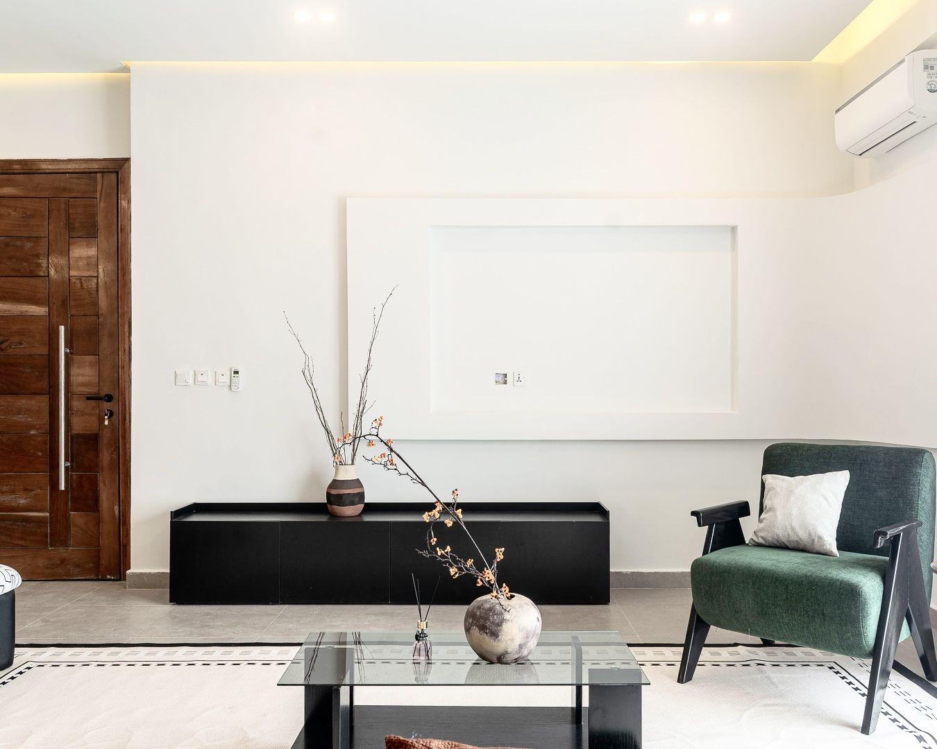 Television wall with a recessed plaster frame, black console and green armchair